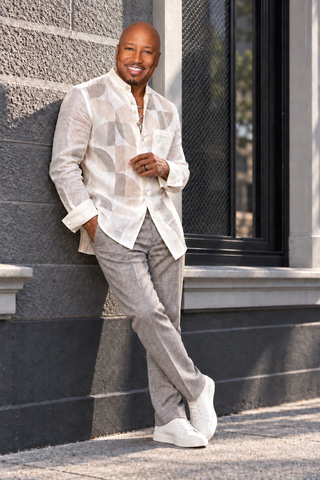 Gather Williams leaning against a stone wall in a cream linen shirt